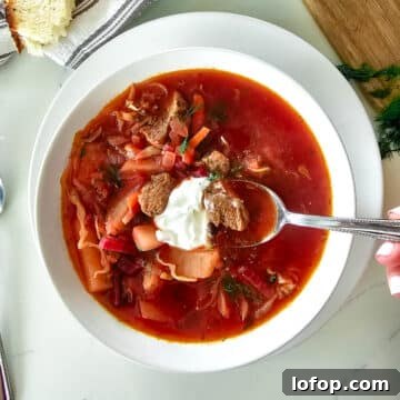 borscht in a white bowl with dollop of sour cream.