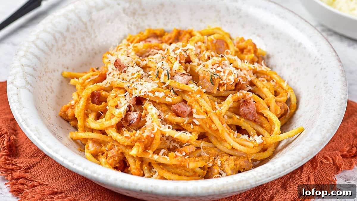12 Flavor-Packed Meatless Dinners You’ll Love Tonight 8 A bowl of spaghetti coated in a creamy orange sauce, topped with grated cheese and small pieces of meat, on a white plate with a textured rim.