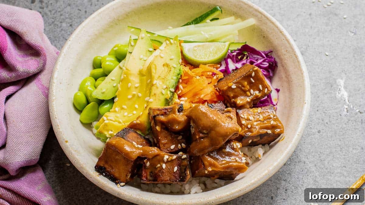 12 Flavor-Packed Meatless Dinners You’ll Love Tonight 10 A bowl with rice, tofu, edamame, avocado, cucumber, shredded carrots, and red cabbage, garnished with sesame seeds and a lime wedge. A pink napkin is on the left side.