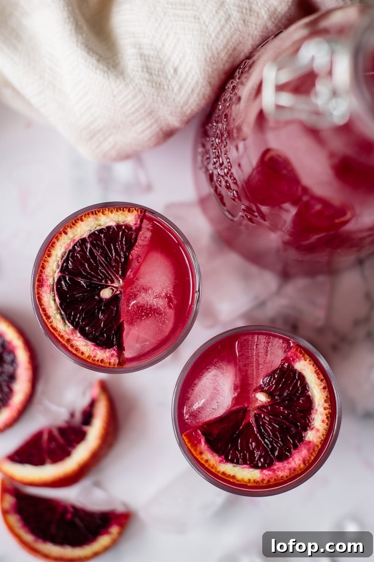 Winter Blood Orange Lemonade Recipe — Refreshing Citrus Drink 5 Blood orange lemonade in two glasses and a pitcher, with ice cubes and slices of orange.