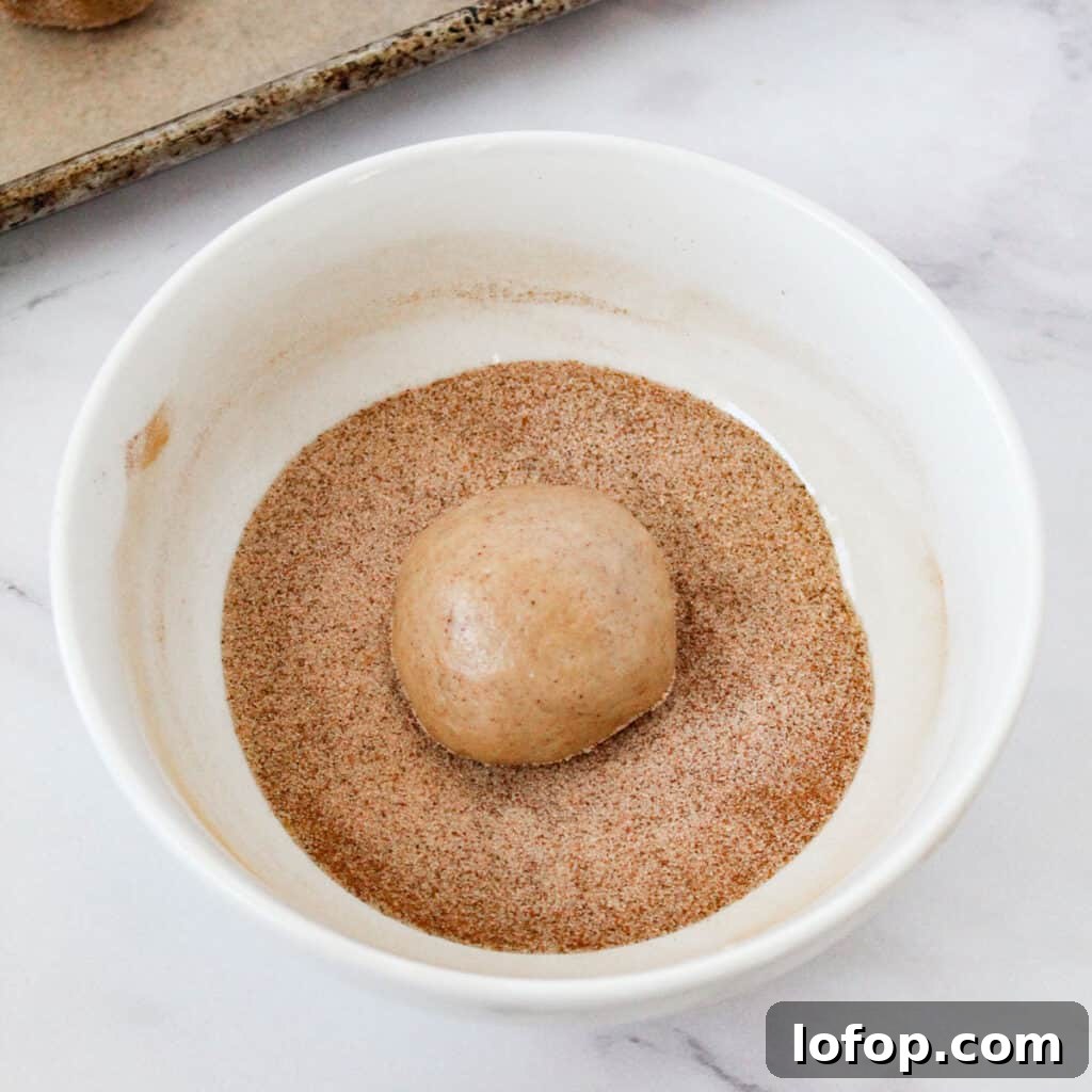 rolling chewy snickerdoodle dough ball in cinnamon sugar