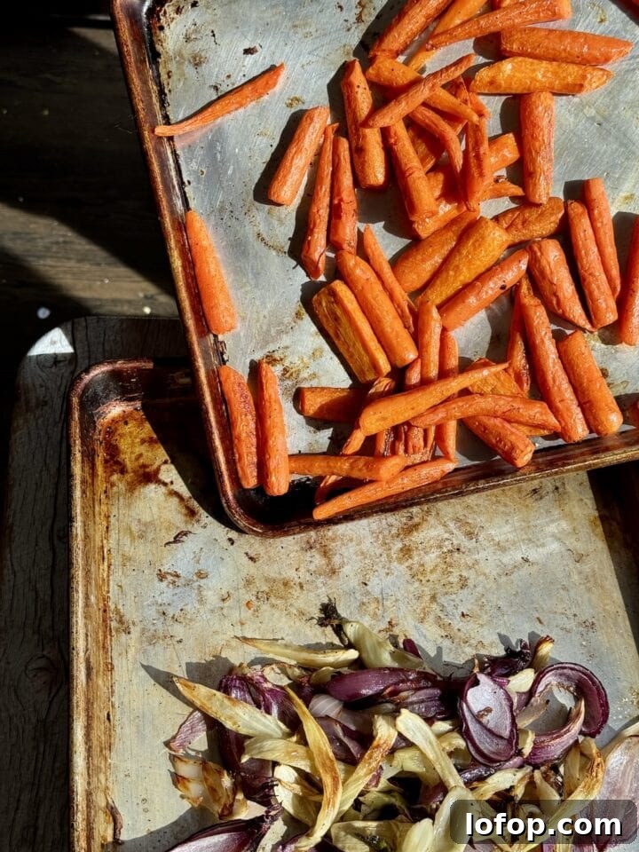 roasted carrots on a sheet pan pouring onto a sheet pan with fennel and onion