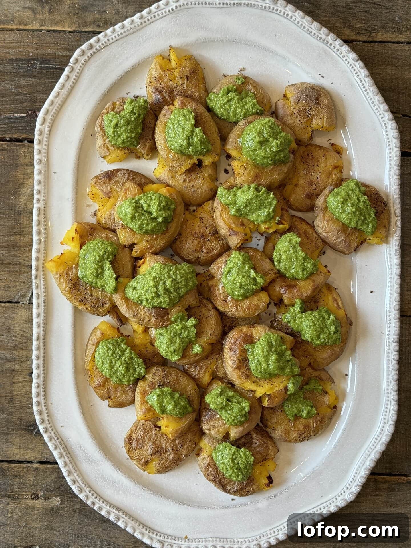 an above view photo of smashed potatoes on a white platter with pesto dolloped on top
