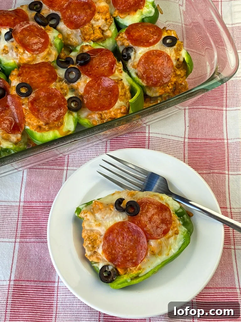 Creamy Pizza-Stuffed Bell Peppers Recipe for Weeknight Dinner 11 White plate with a green pepper covered in pepperonis, melted cheese, sliced olives and filled with a creamy, meaty mixture with a fork