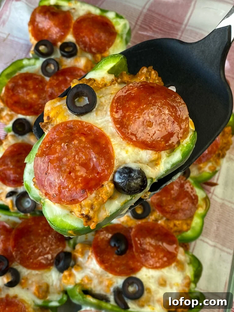 Creamy Pizza-Stuffed Bell Peppers Recipe for Weeknight Dinner 3 Spatula lifting up a stuffed pizza pepper with a green pepper crust above a big pan of stuffed peppers