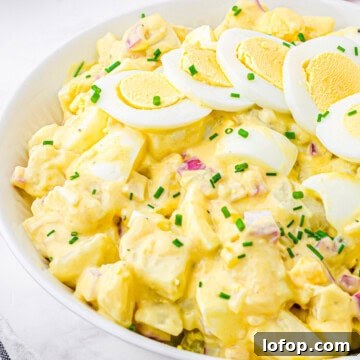Square up close image of Classic Potato Salad in white bowl with hard-boiled eggs and chives for garnish