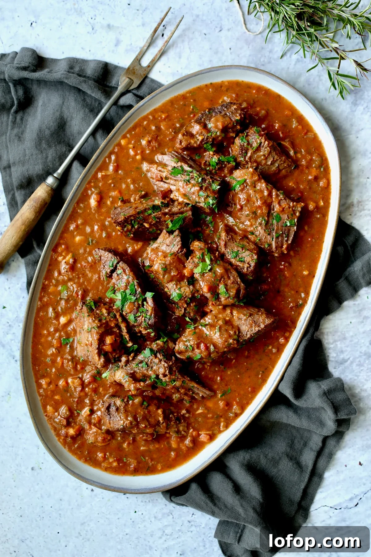 Authentic Stracotto: Italian Pot Roast Recipe for Slow-Cooked Beef 8 Italian Pot Roast (Stracotto) broken into pieces on oval gray-rimmed platter with meat fork.