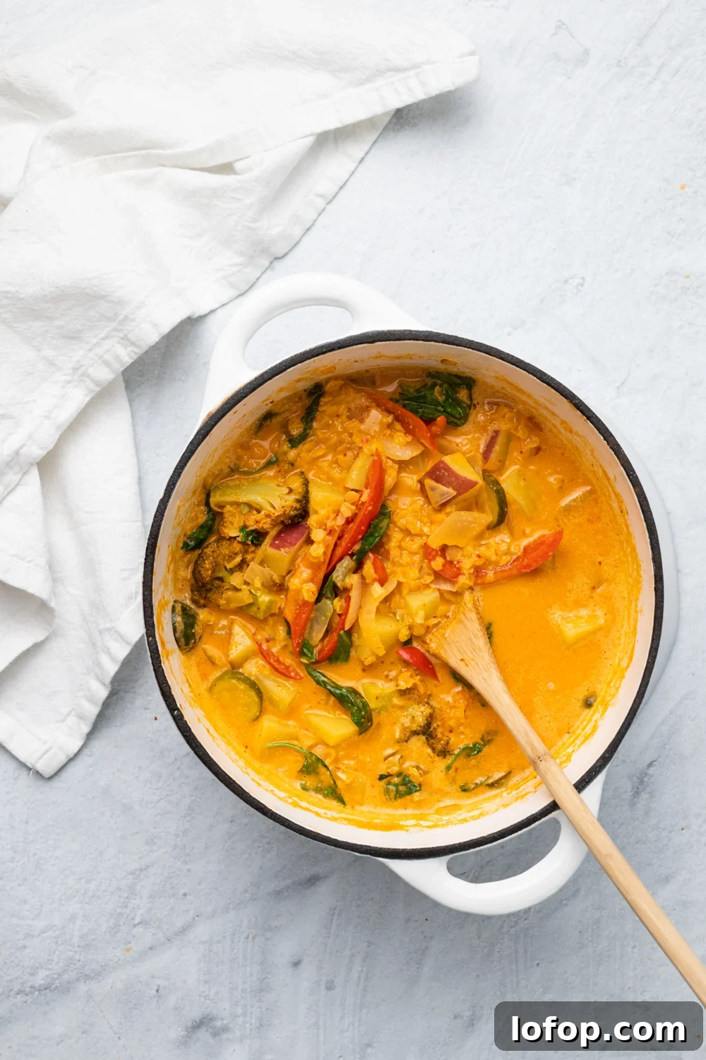overhead shot of a white ceramic pot filled with vegan red lentil sweet potato curry