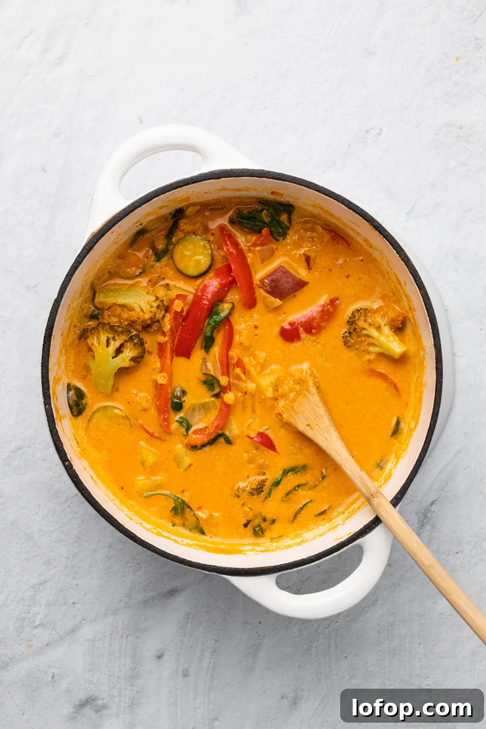 overhead shot of a pot of vegan red lentil sweet potato curry in a white pot with a wooden spoon