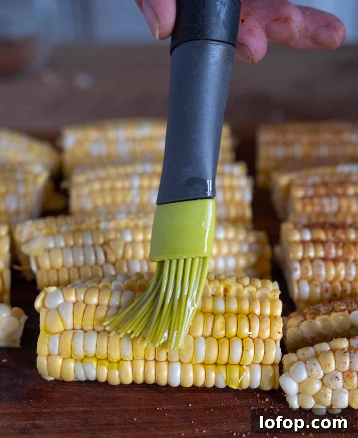 Brushing olive oil over prepared corn.