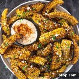 Corn Ribs with dipping sauce sitting in a plate sprinkled with cotija cheese.
