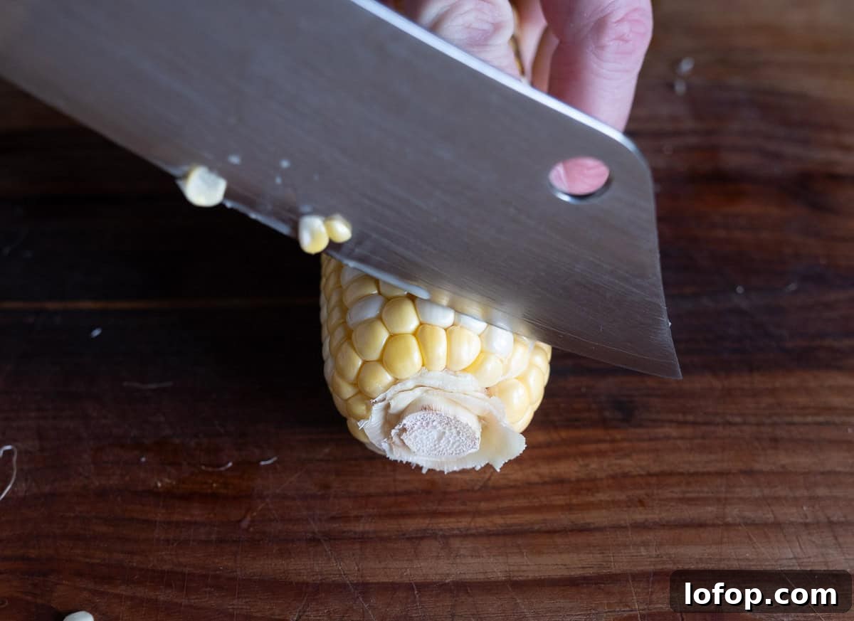 Removing the stem end of a corn cob with a sharp knife.
