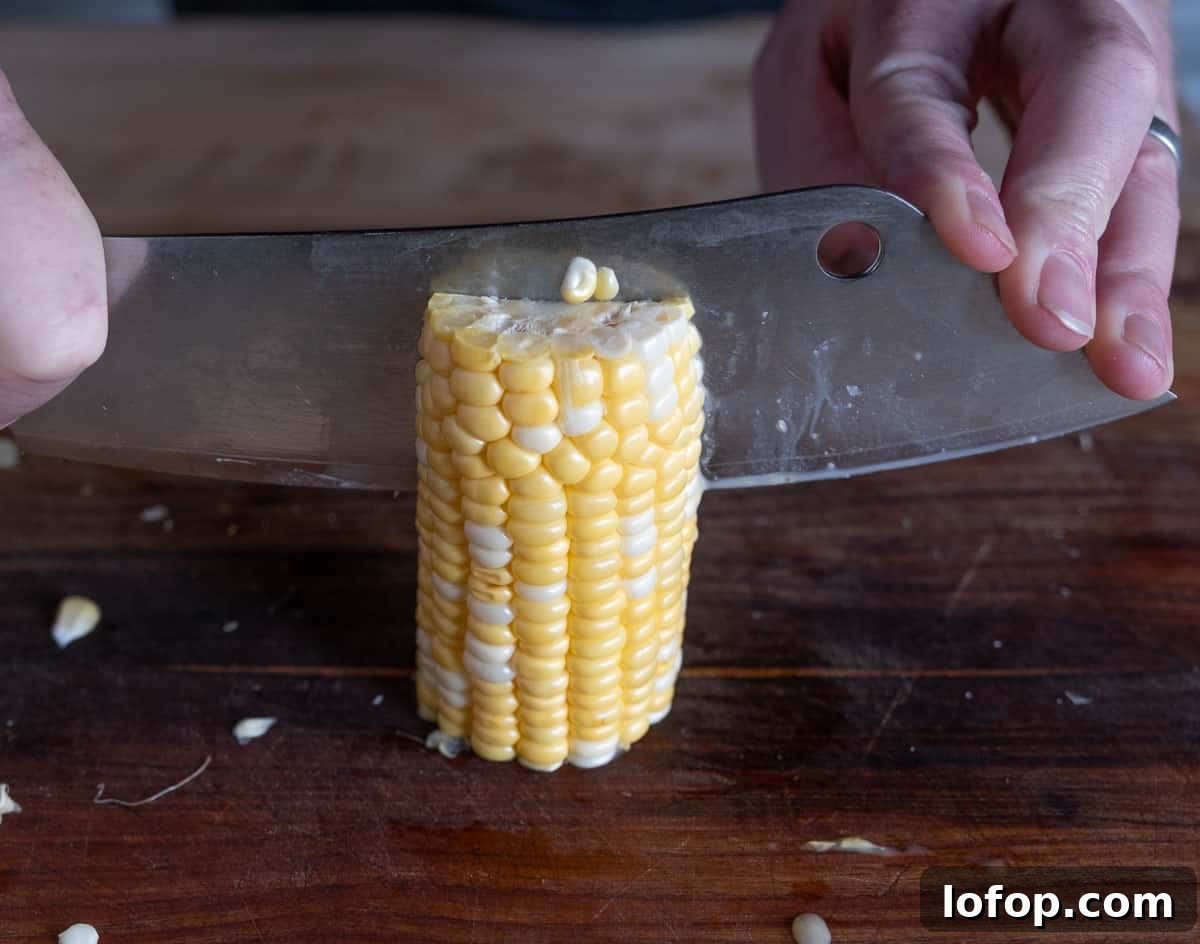 Standing up half of a corn cob and cutting in half.