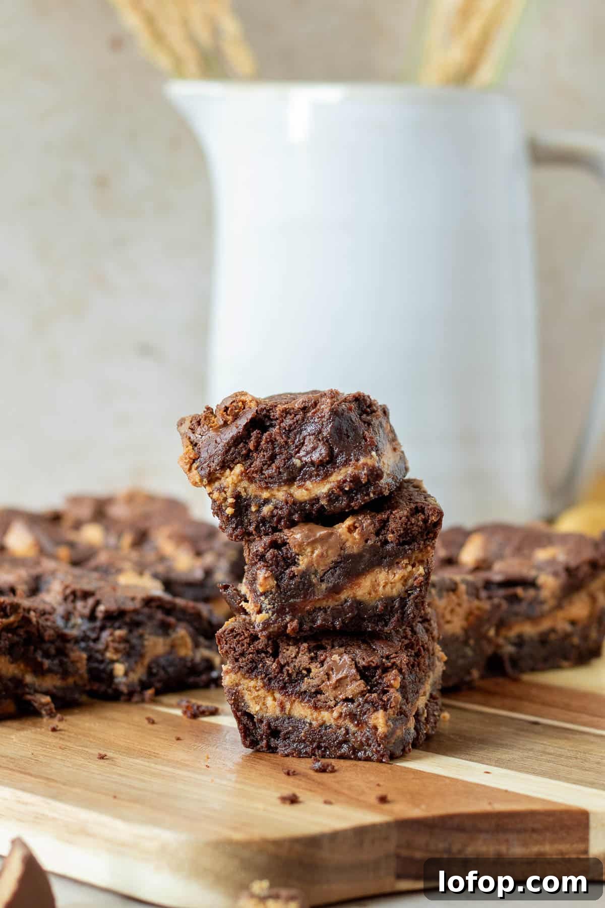 Decadent Peanut Butter Cup Fudgy Brownies Recipe 2 stack of chocolate peanut butter cup brownies on a wood cutting board with a white picture in the background