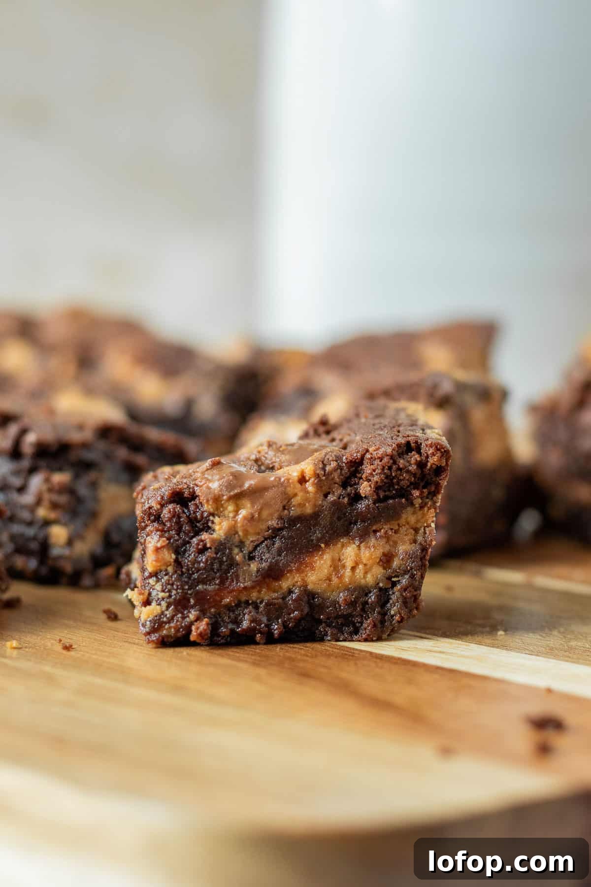 Decadent Peanut Butter Cup Fudgy Brownies Recipe 7 close up of a brownie with a peanut butter layer and peanut butter cups sitting on a wood board