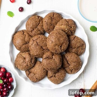 Soft and chewy ginger cookies shown in a serving dish surrounded by cranberries and cinnamon sticks.