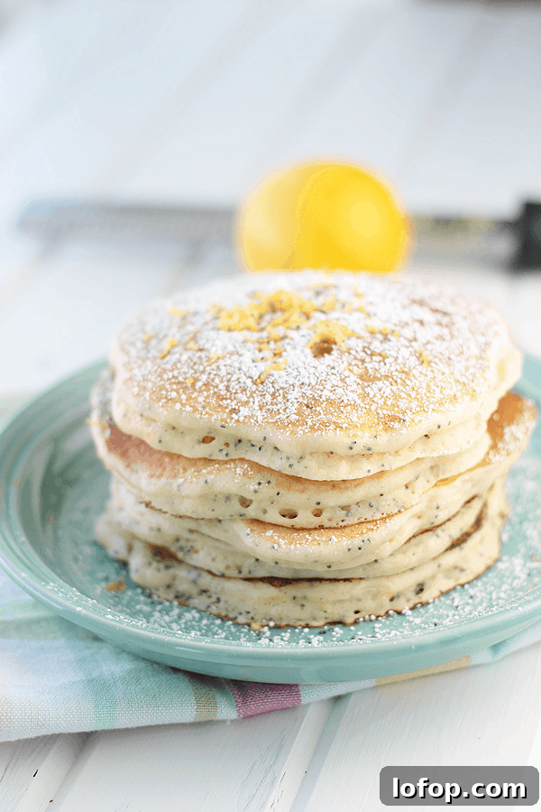 Fluffy Lemon Ricotta Pancakes with Honey & Blueberry Topping 2 stack of lemon ricotta pancakes on a blue plate with powdered sugar and lemon zest on top