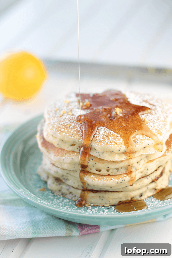 Fluffy Lemon Ricotta Pancakes with Honey & Blueberry Topping 3 a stack of lemon ricotta pancakes on a blue plate with powdered sugar, lemon zest, and some maple syrup being drizzled over the top