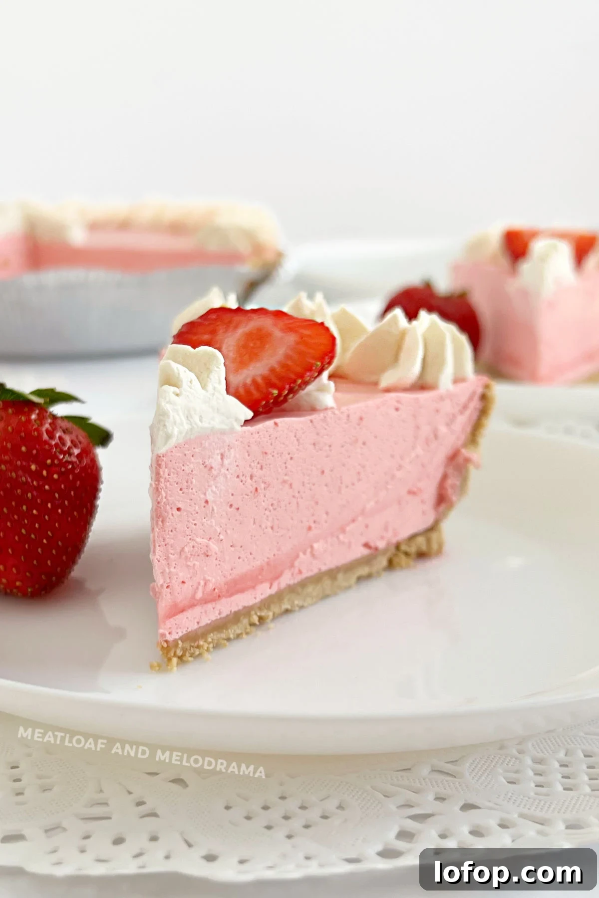 slice of no bake strawberry jello pie with cool whip, strawberries and whipped cream on plate