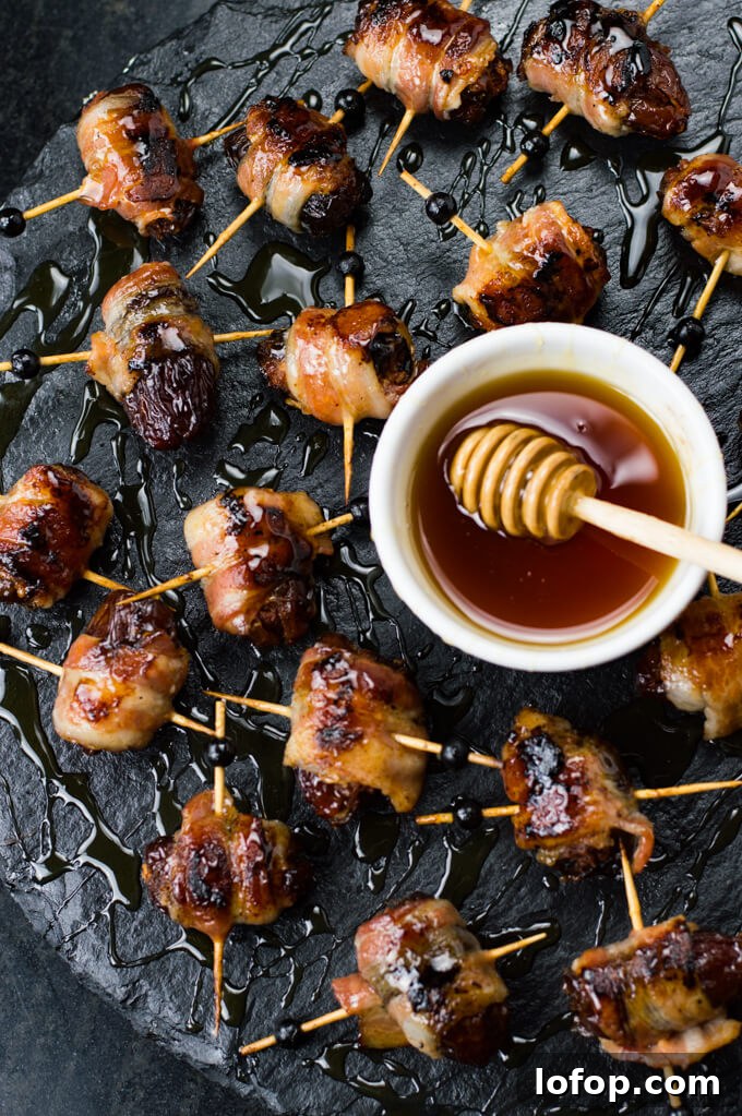 Bacon-Wrapped Stuffed Dates with Goat Cheese and Almonds 2 Bacon wrapped chorizo stuffed dates scattered on a black serving tray. A white bowl of honey with a honey drizzler in it.