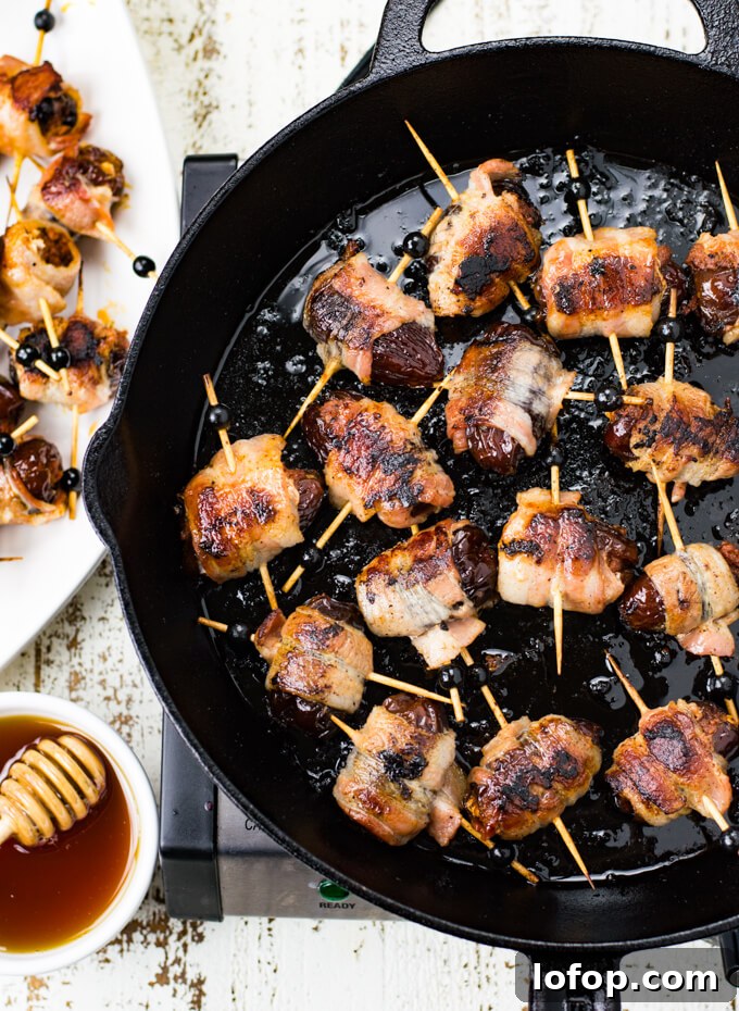 Bacon-Wrapped Stuffed Dates with Goat Cheese and Almonds 6 A black cast iron skillet holds cooked bacon wrapped dates stuffed with chorizo. A bowl of honey and a drizzler sits next to it.