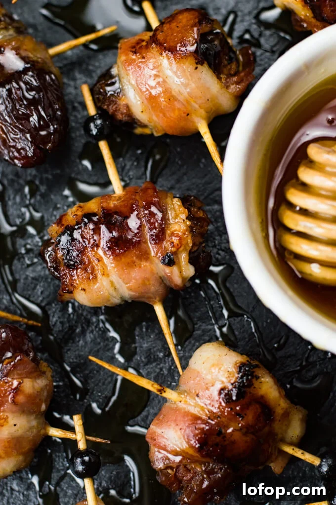 Bacon-Wrapped Stuffed Dates with Goat Cheese and Almonds 8 A close-up of dates that are stuffed with chorizo and wrapped in bacon. A small bowl of honey sits next to them.