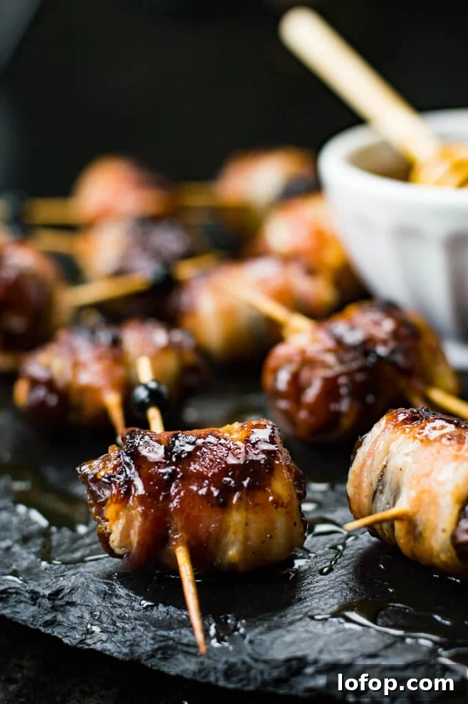 Bacon-Wrapped Stuffed Dates with Goat Cheese and Almonds 9 A close-up of dates that are stuffed with chorizo and wrapped in bacon. A small bowl of honey sits next to them.