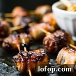 A close-up of dates that are stuffed with chorizo and wrapped in bacon. A small bowl of honey sits next to them.