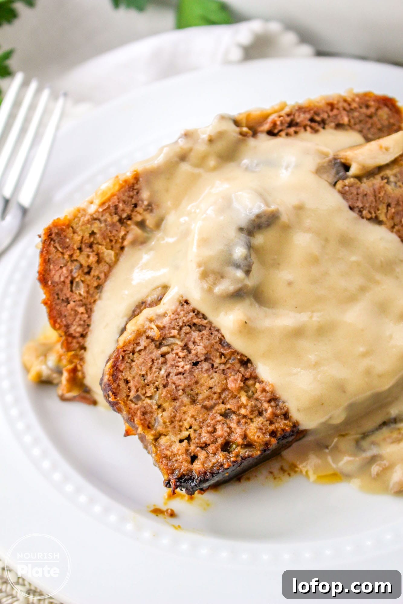 Savory Mushroom Meatloaf with Rich Mushroom Gravy 11 Close up shot of mushroom meatloaf slices with gravy on a white plate