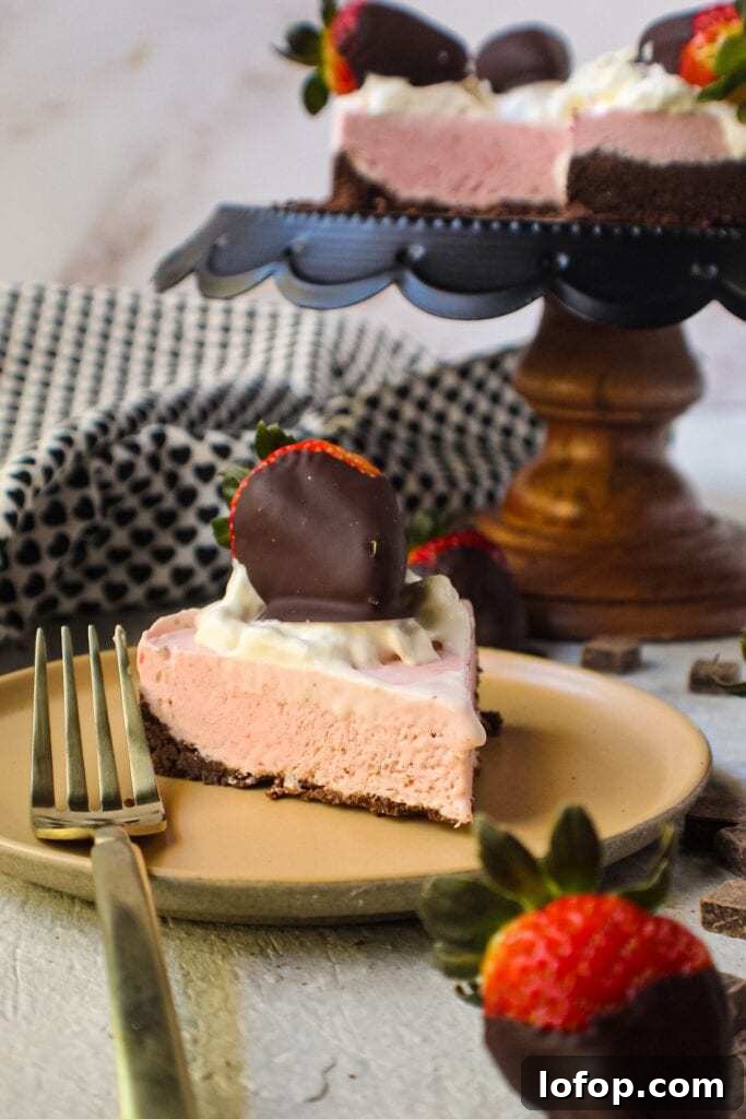No-Bake Chocolate Strawberry Cheesecake Recipe for Summer 4 chocolate strawberry no-bake cheesecake slice on tan plate with whole cheesecake on cake stand in background topped with whipped cream and strawberries