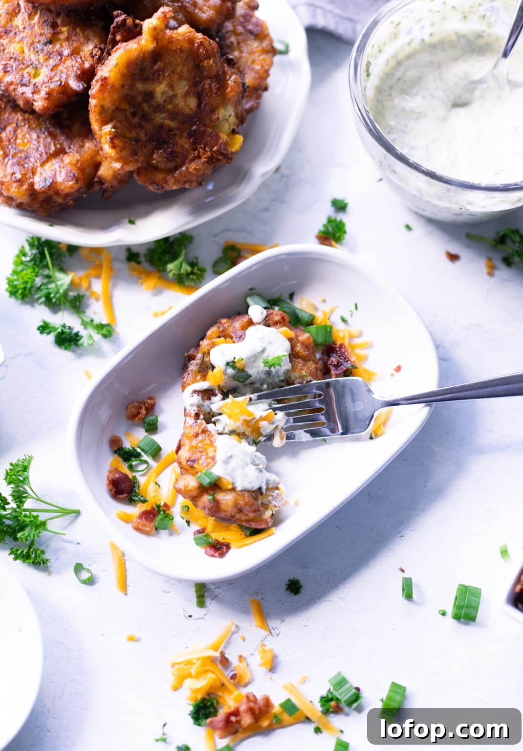 Person eating corn fritters in a white dish with a fork.
