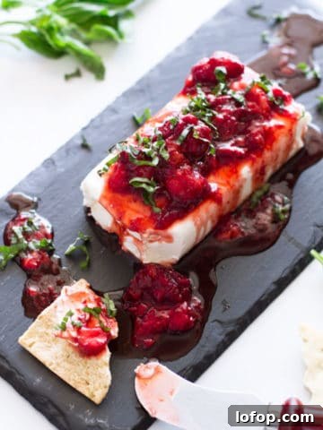 Cream cheese with strawberry sauce topped with basil, pita chip on table.