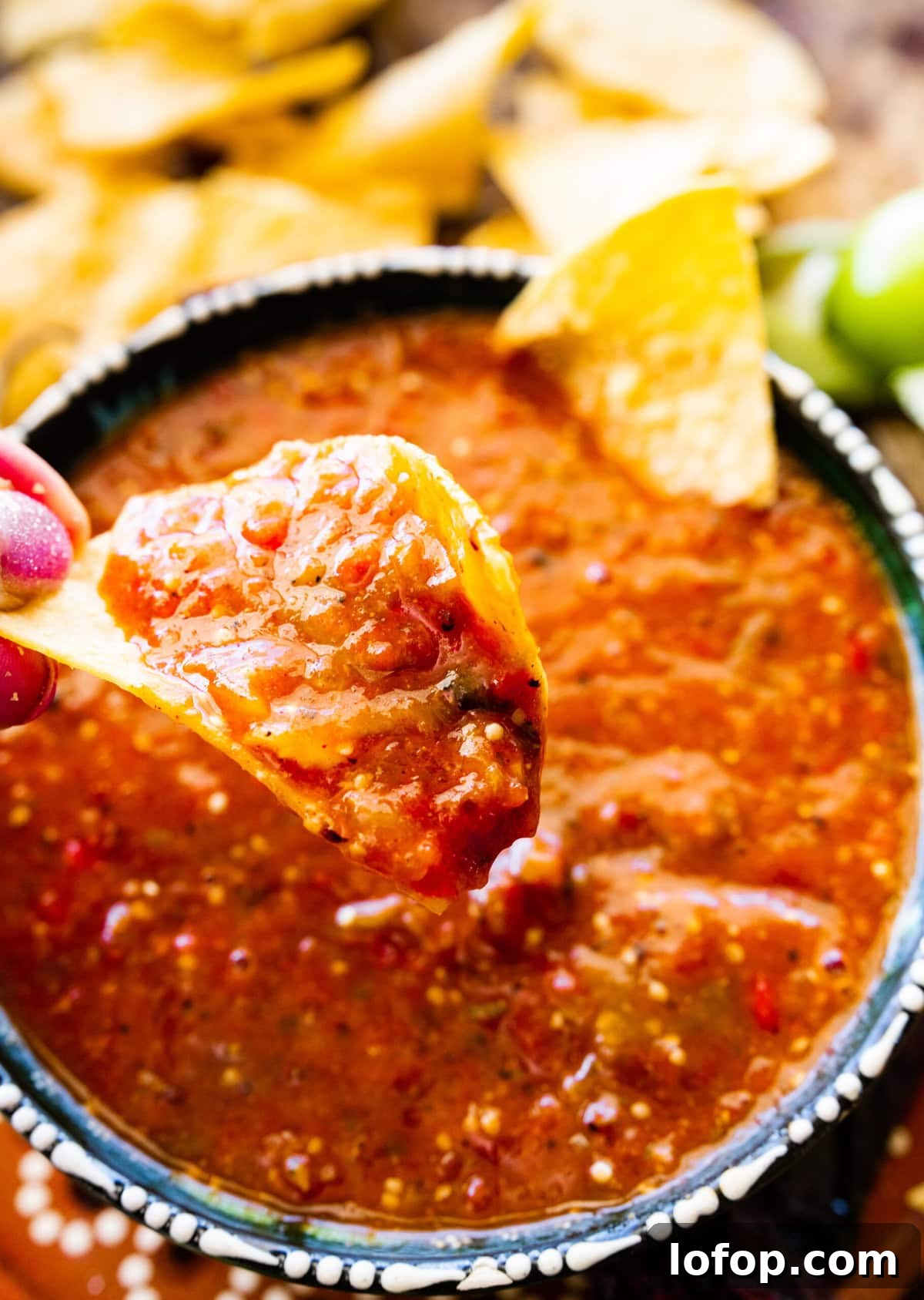 Copycat Chipotle Red Chili Salsa Recipe: Authentic Hot Salsa 12 Hand holding a chip dipped in copycat Chipotle hot salsa over a bowl.
