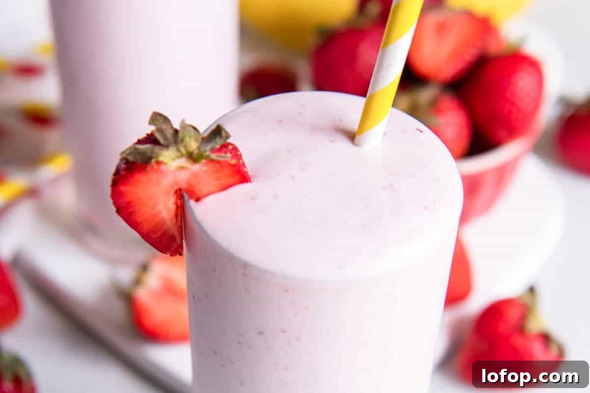 A pink strawberry banana smoothie with a striped straw.