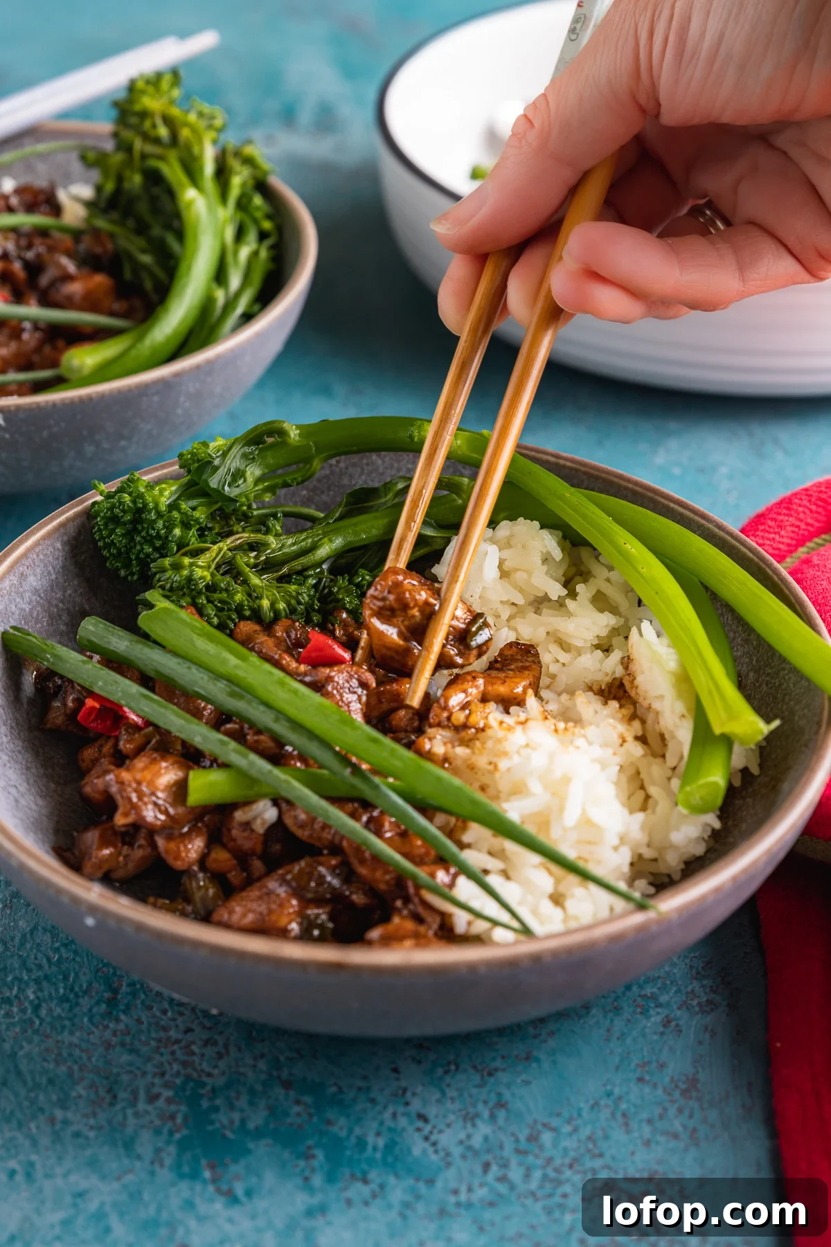 15-Minute Shanghai-Style Chicken Stir-Fry Recipe 2 Someone eating Shanghai chicken with rice with chopsticks from a blue grey bowl on a blue background