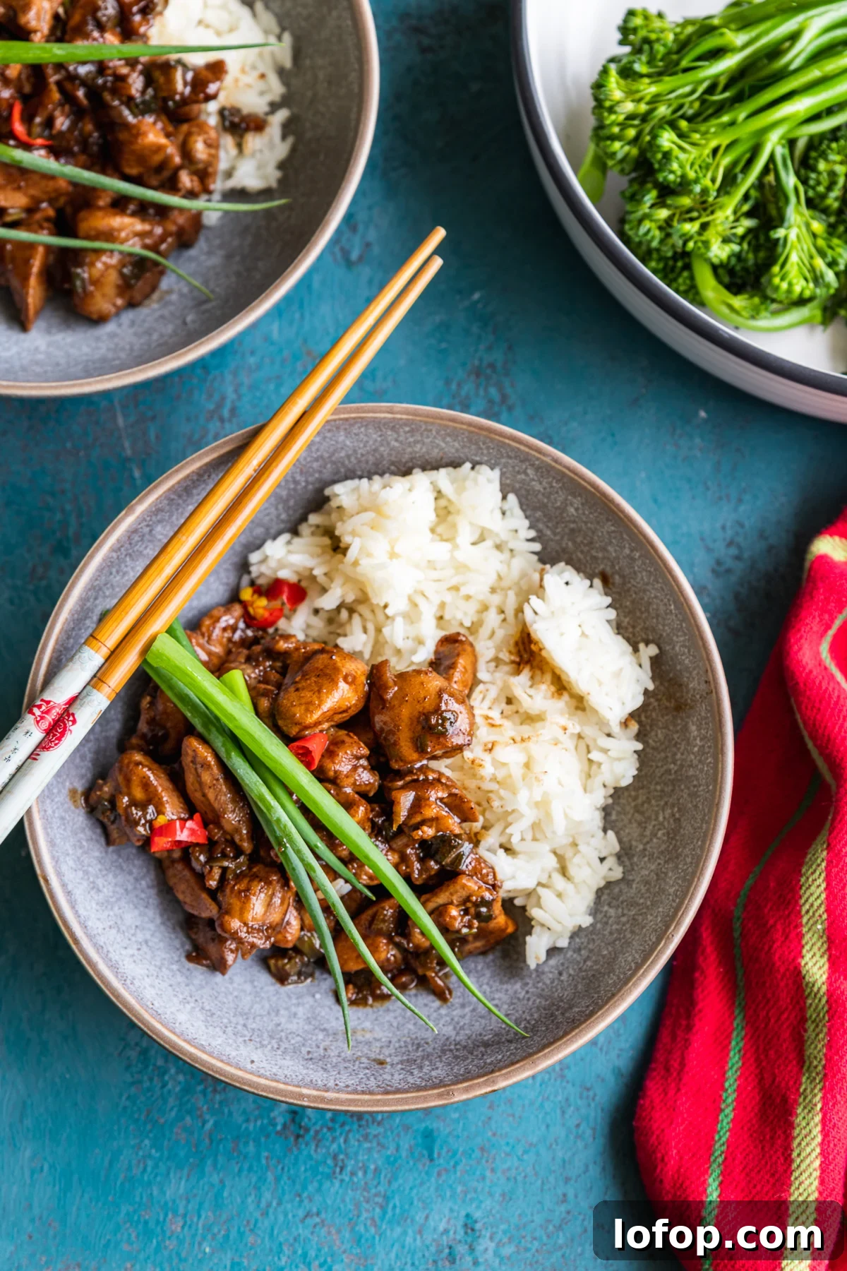 15-Minute Shanghai-Style Chicken Stir-Fry Recipe 6 A dish of Shanghai chicken with chopsticks laid over the top from above on a blue background and with a red stripy tea towel