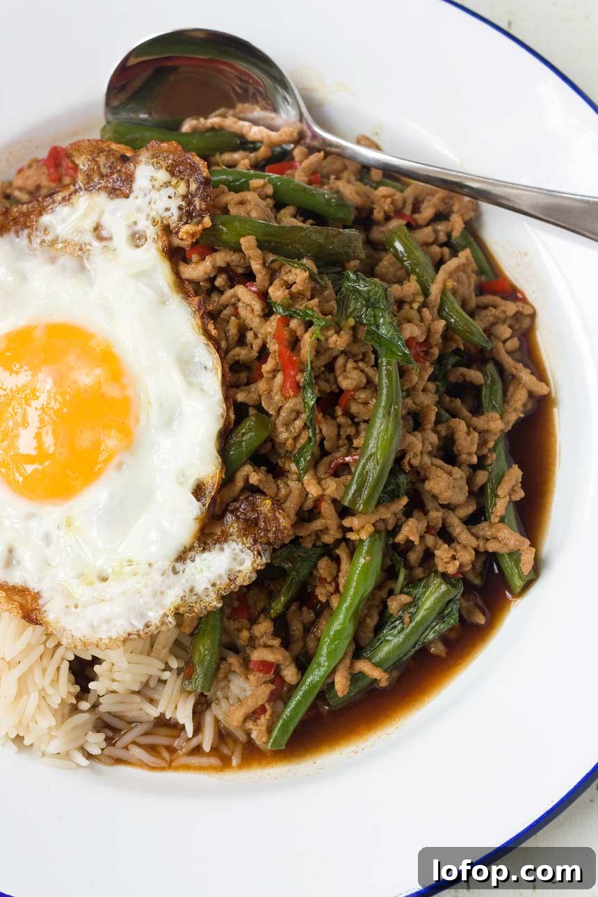 15-Minute Shanghai-Style Chicken Stir-Fry Recipe 8 A Thai basil stir-fry from above on a white plate with an egg on top and a spoon on the plate