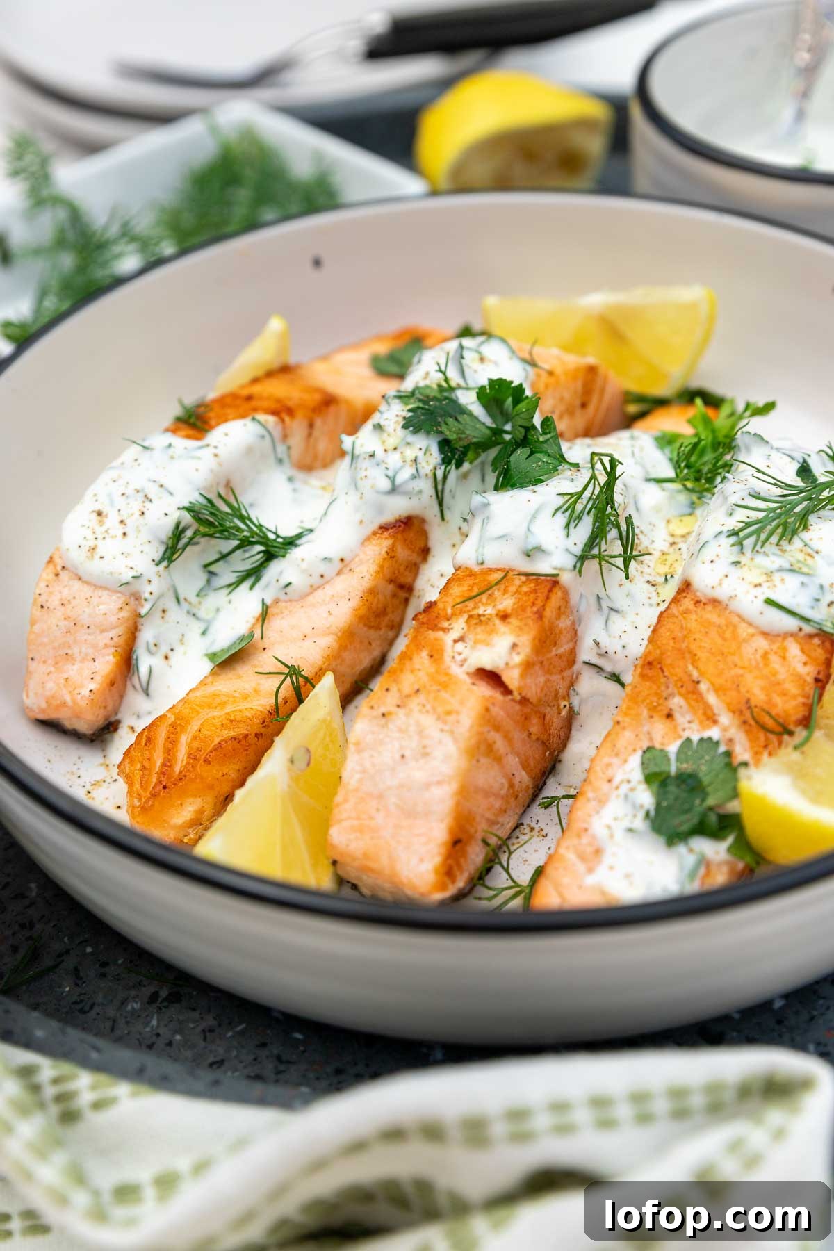 15-Minute Shanghai-Style Chicken Stir-Fry Recipe 10 Closeup of a dish of cooked salmon with dill yogurt sauce drizzled over it garnished with lemon segments and herbs and with a green and cream tea towel at the side.