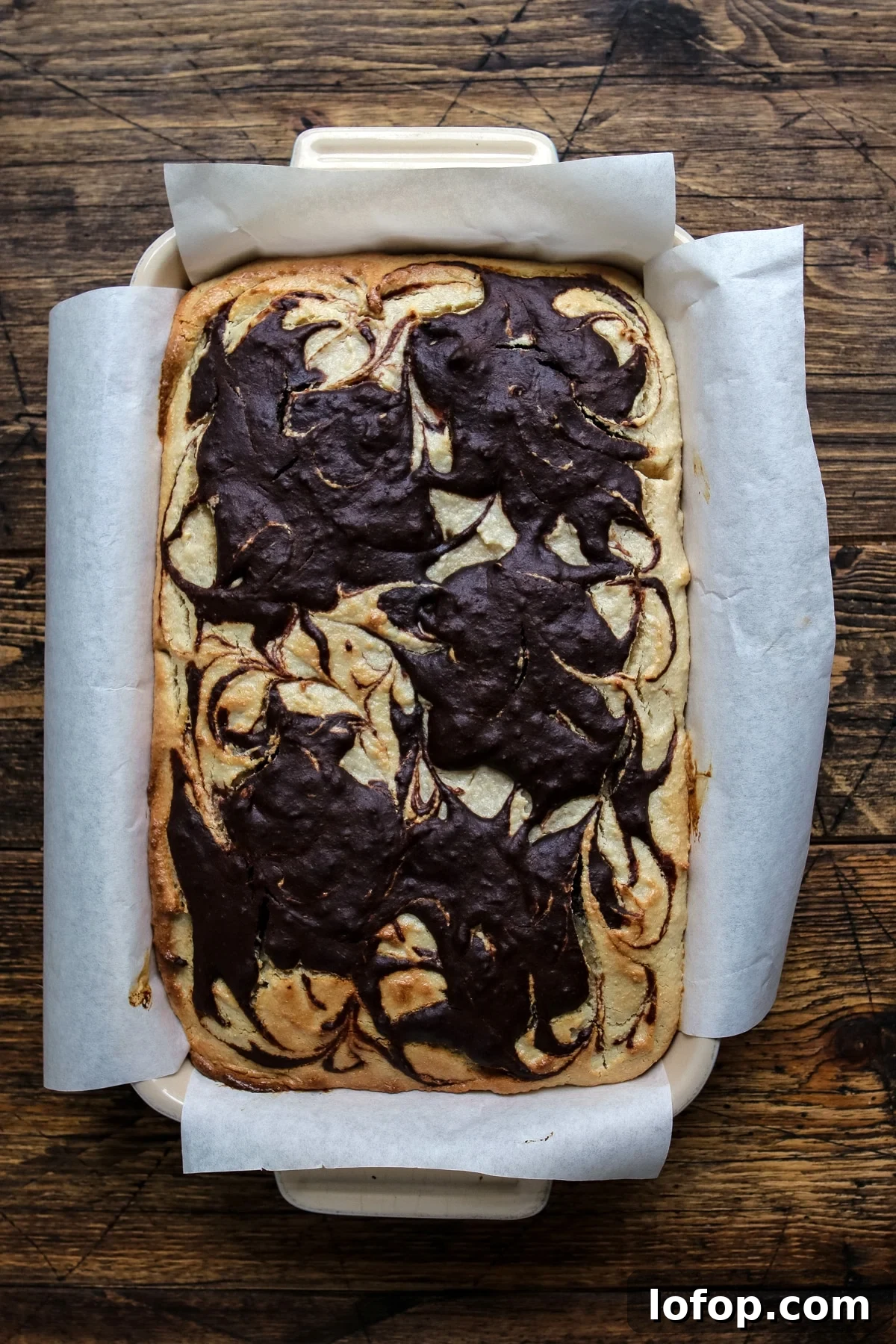 A square pan featuring a dessert with glossy chocolate swirls artistically arranged on top.