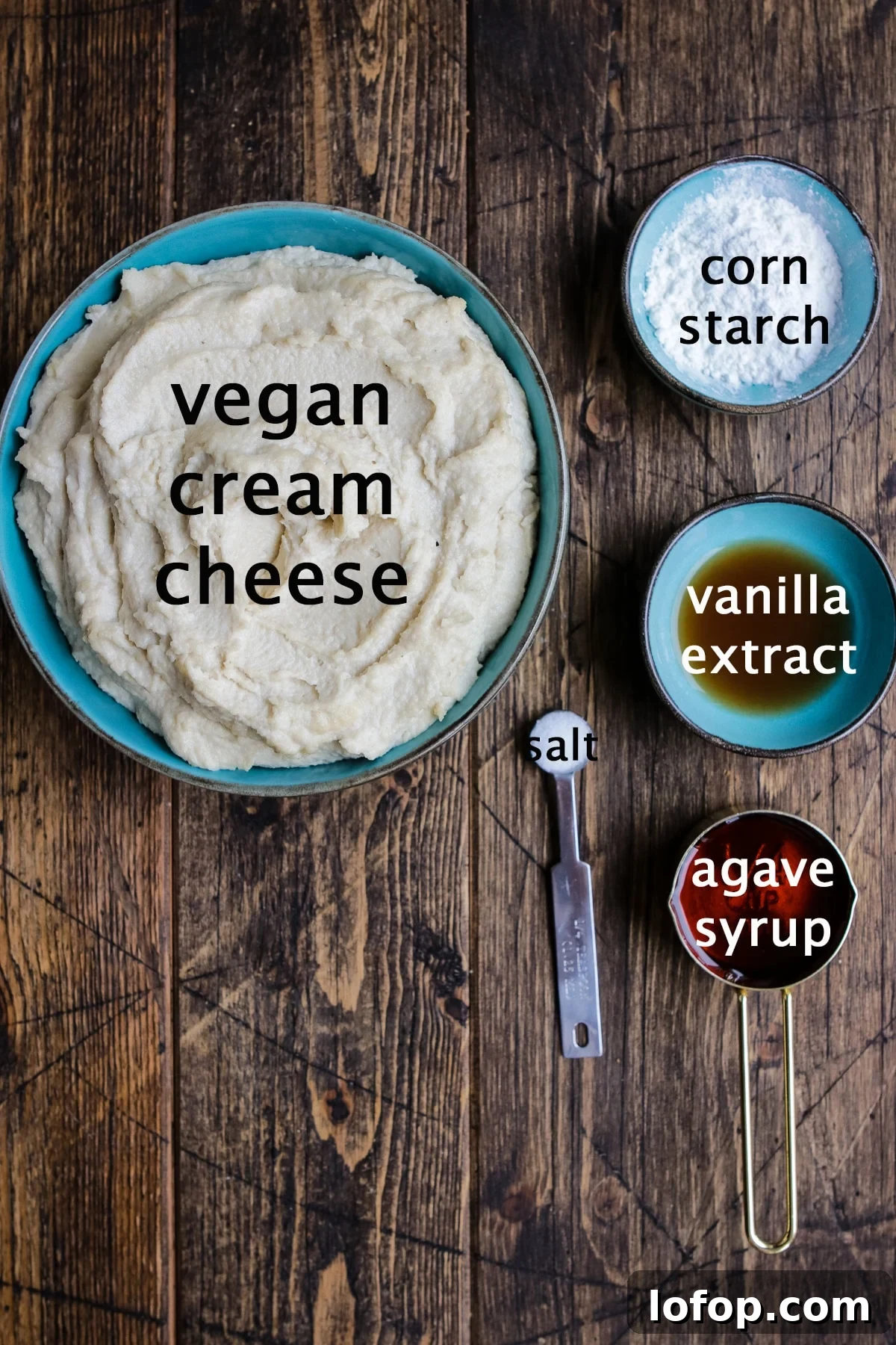 Vegan cheesecake layer for cheesecake brownies with ingredients like vegan cream cheese, corn starch, vanilla extract, agave syrup, and salt displayed on a wooden countertop.