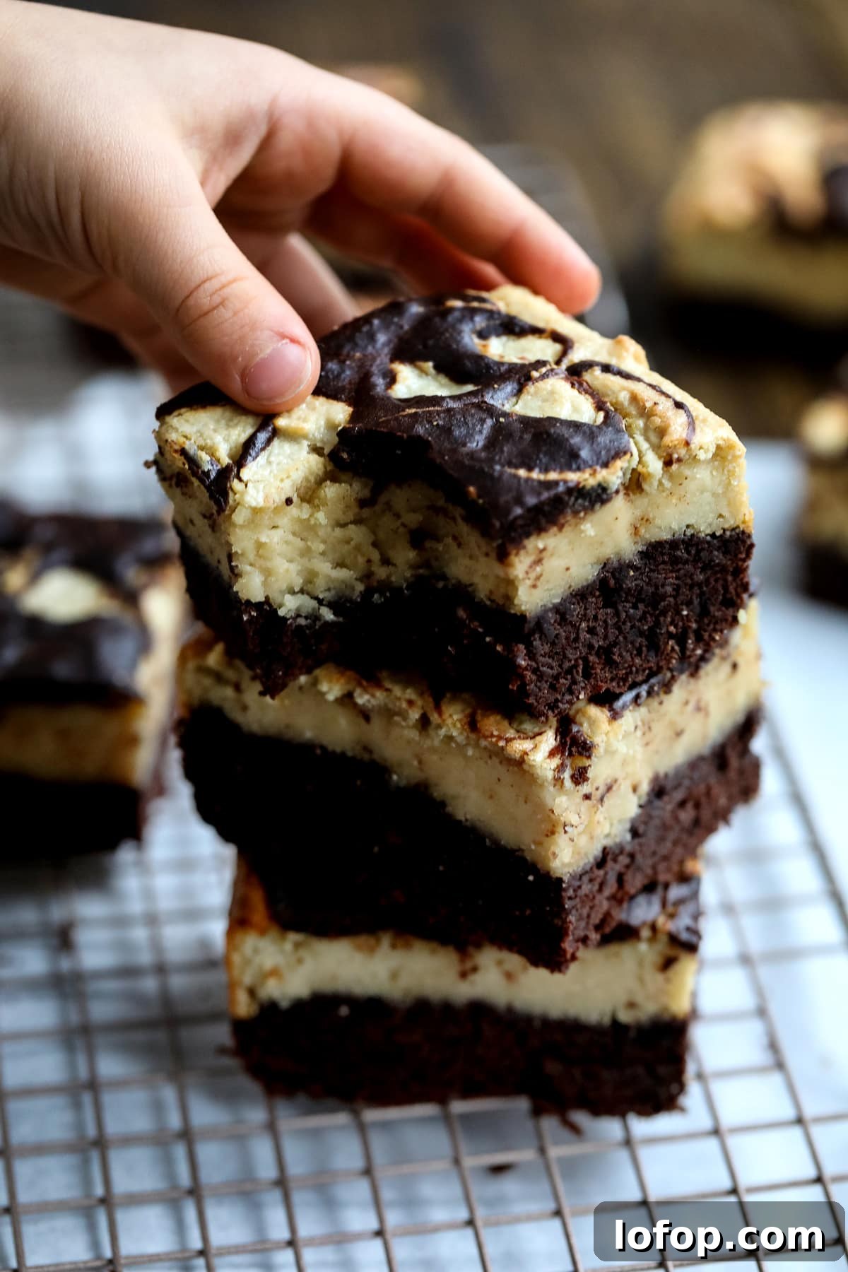 A hand extends towards a rich, chocolate brownie on a plate, ready to take a piece.