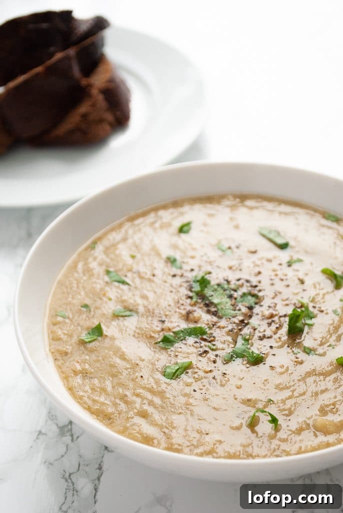 Roasted Broccoli Soup Recipe: Creamy Oven-Roasted Broccoli Bowl 2 A bowl of roasted broccoli soup with a plate of pumpernickel bread in the background.