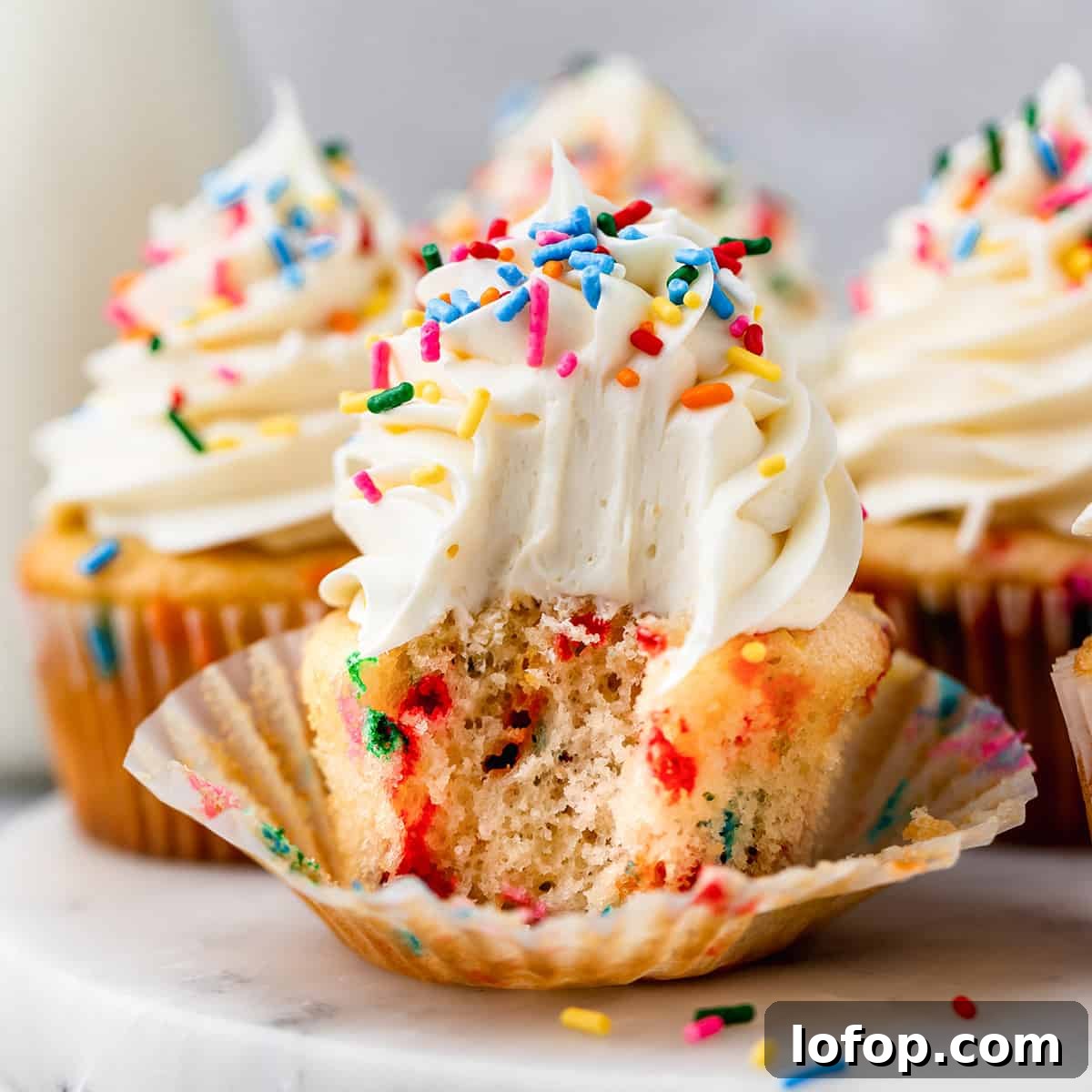 Funfetti Cupcake with vanilla frosting and sprinkles & a bite taken out of it
