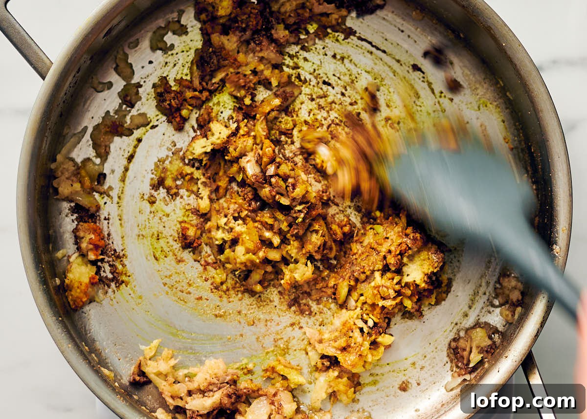 Sauteeing onions and spices in a pan for vegetarian butter chicken recipe.