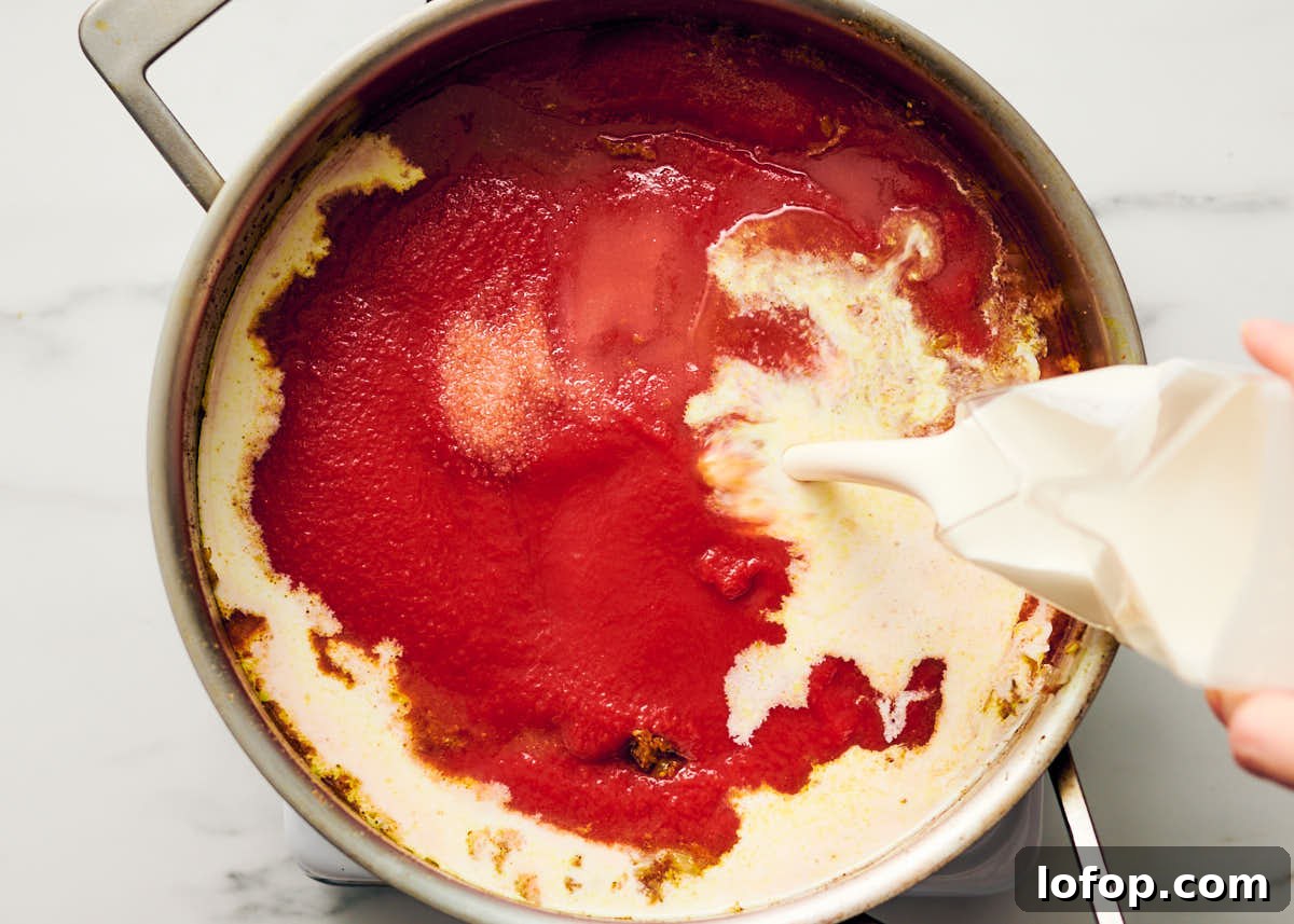 Pouring cream into a pan of passata and spices for vegetarian butter chicken.