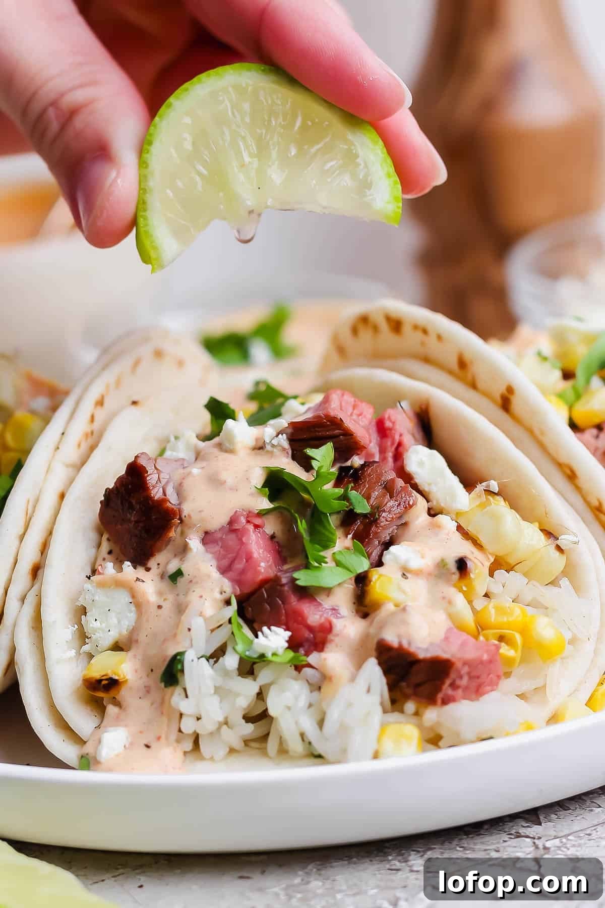 Grilled Steak Tacos with Chipotle-Lime Sauce 6 A hand squeezing a lime wedge over a grilled steak taco.