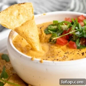 Dipping a tortilla chip into vegan queso