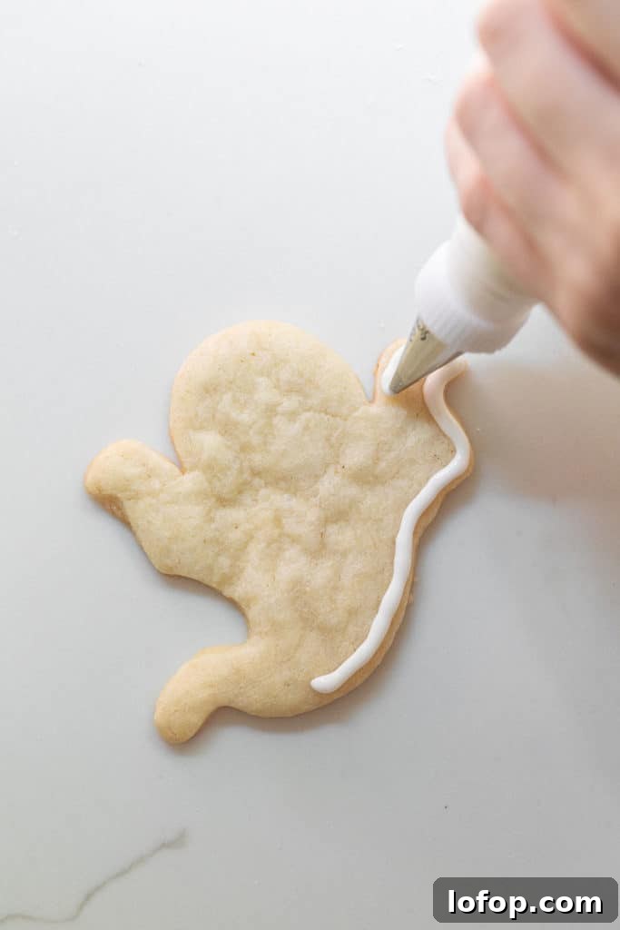 Spooky Halloween Sugar Cookie Recipe for Festive Treats 9 Piping royal icing on a Halloween sugar cookie ghost.