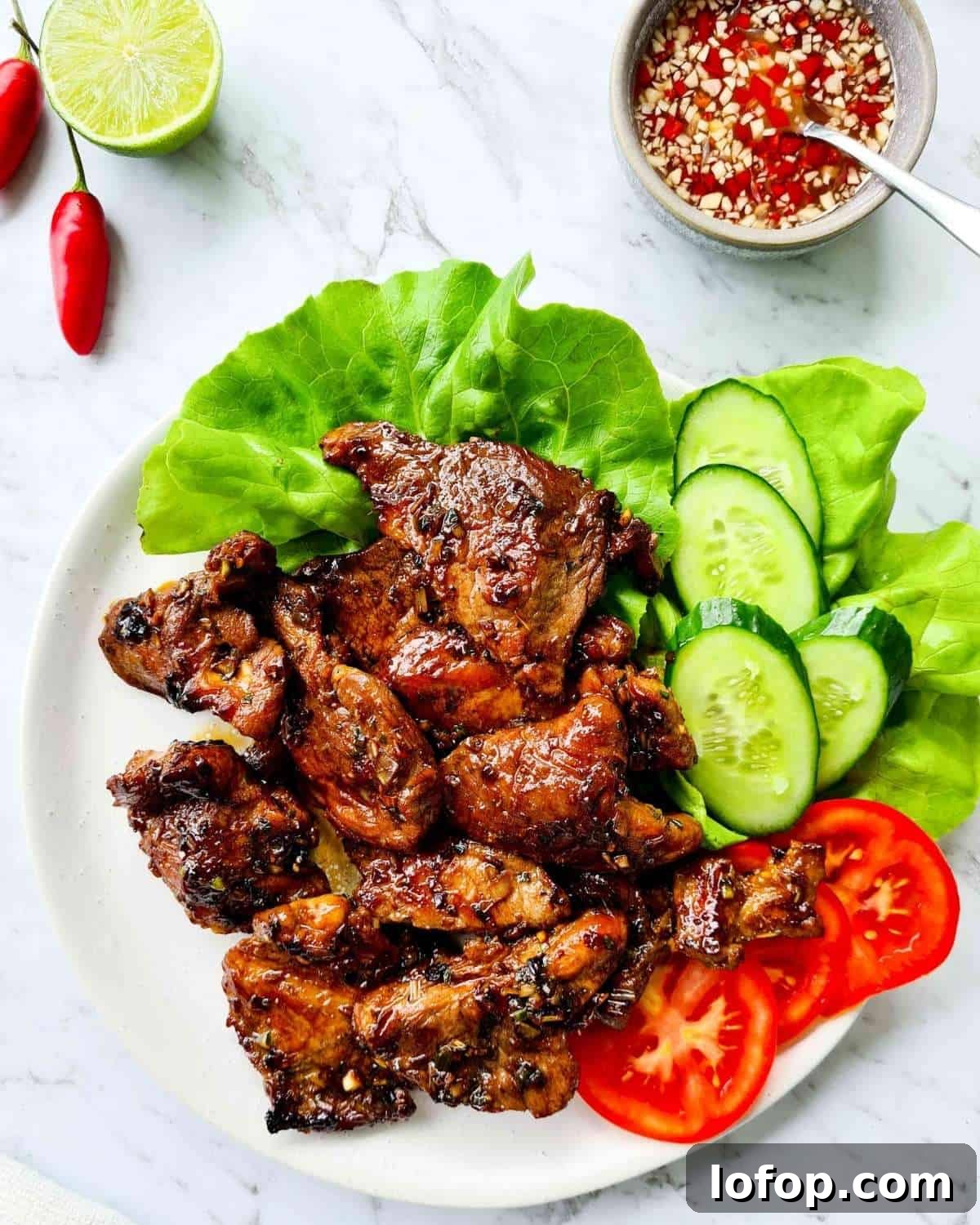 A large plate of cooked Vietnamese pork chops with fresh lettuce, cucumber and tomato slices.