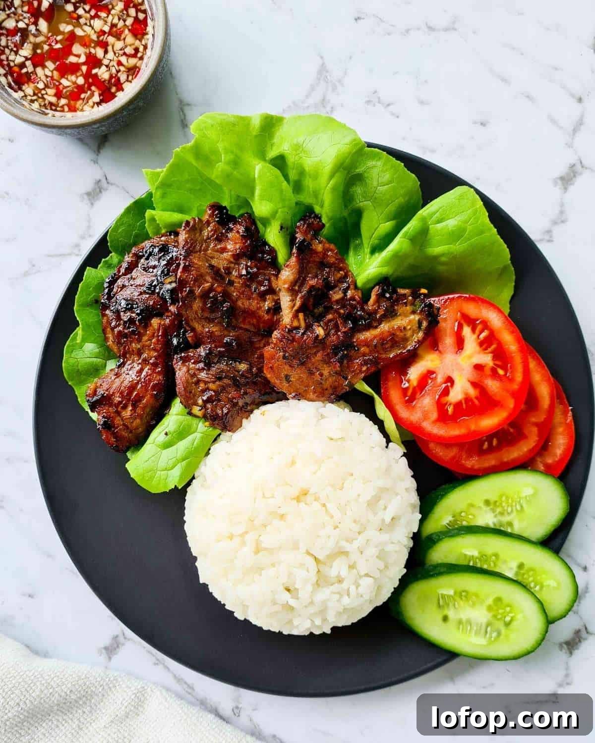 Lightly charred pork with rice, fresh tomatoes and cucumber slices on a black plate